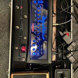 V hliníkovém kufru se nachází černý kytarový procesor s modře podsvíceným panelem a nápisem Hughes & Kettner Black Spirit 200. Zařízení obsahuje řadu…