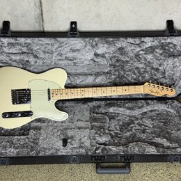 Elektrická kytara typu Telecaster v krémové barvě s bílým pickguardem, uložená v černém tvrdém kufru s šedou polstrováním. Na hlavě hmatníku je vidit…
