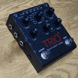 Černý kytarový pedál s nápisy TRIO+ a Band Creator+ Looper. Zařízení obsahuje několik ovládacích knoflíků, přepínačů a sekci s označením GENRE, STYLE…