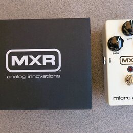 Bílá kytarový efekt pedál s nápisy MXR a micro amp +. Pedál má tři černé ovládací knoflíky s popisky GAIN, BASS a TREBLE, červenou kontrolku a stomeč…