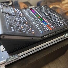 Černý digitální mixážní pult s displejem a množstvím posuvníků, knoflíků a barevných tlačítek. Na pravém předním okraku je bílý nápis MIDAS. Zařízení…