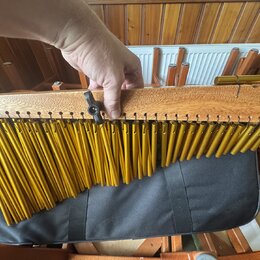 Detailní pohled na kalimbu s dřevěným rezonátorem světlé barvy a kovovými plátky zlaté barvy. Na pravém konci dřevěné části je vyryto logo ve tvaru s…
