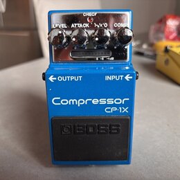 Modrý efekt pedál s nápisy Compressor a CP-1X. Na horní části jsou čtyři ovládací knoflíky s popisky LEVEL, ATTACK, 'V'O a COMP, kontrolka CHECK a př…