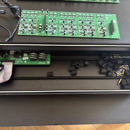 Fotografie zobrazuje dvě zelené elektronické desky s osazenými součástkami a černý obdélníkový šasi z tmavého dřeva. Na jedné z desek je vidět nápis…