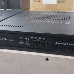 Černý rackový zesilovač s nápisem LUCIA 240/2M a logem LAB.GRUPPEN. Na předním panelu jsou dva ovratové ovládací knoflíky s označením -INF, 0 a -10dB…