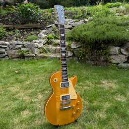 Elektrická kytara typu Les Paul v žluté barvě s viditnou strukturou dřeva. Na hlavě hmatníku je nápis Gibson a na krytce krku je vidět logo. Nástroj…
