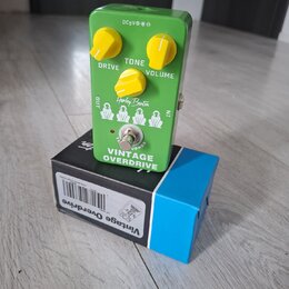 Zelený efekt pedál s nápisem Vintage OVERDRIVE a logem Harley Benton. Má tři žluté oválné ovladače s popisky DRIVE, TONE a VOLUME. Na horní straně je…