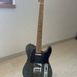 Elektrická kytara typu Telecaster s tmavě šedým trupem s viditnou strukturou dřeva a černým pickguardem. Hmatník a hlava jsou vyrobeny ze světlého dř…