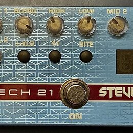Modře barevný basový předzesilovač s bílým grafickým vzorem Union Jack a texturou v podobě mřížky. Na přístroji jsou nápisy TECH 21 a STEVE HARRIS, d…