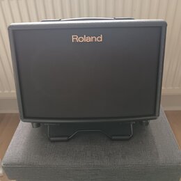 Černý kytarový kombozesilovač s texturovaným povrchem a černou přední síťovkou. V horní části je umístěno bílé logo Roland. Nástroj stojí na černém k…