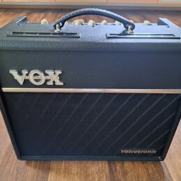 Černý kytarový kombozesilovač s povrchem z texturovaného vinylu a nápisem VOX v chromovém provedení na přední straně. V pravém dolním rohu je bílý ná…