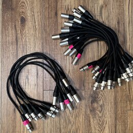 Sada černých audio kabelů s kovovými konektory typu XLR. Některé konektory mají přilepené růžové papírové štítky s ručně psanými označením, například…