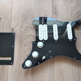 Černý plastový pickguard pro elektrickou kytaru s třemi bílými jednoznačkovými snímači. Na povrchu jsou tři bílé oválné knofíky s nápisy VOLUME, TONE…