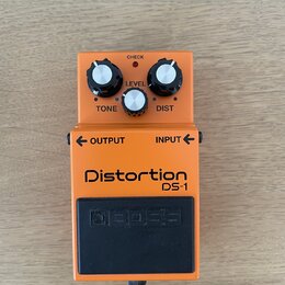 Oranžový efekt pedál s černým stoupacím spínačem. Na zařízení jsou nápisy Distortion DS-1, BOSS, LEVEL, TONE, DIST, CHECK, OUTPUT a INPUT. Povrch ped…