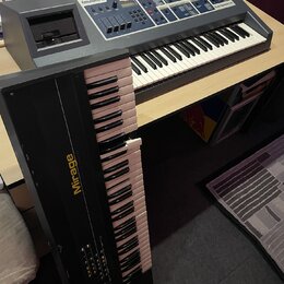 Na fotografii jsou dva klávesové syntezátory. V horní části je šedý přístroj s nápisy Emulator II a E-mu Systems, inc., který má v horní části ovláda…