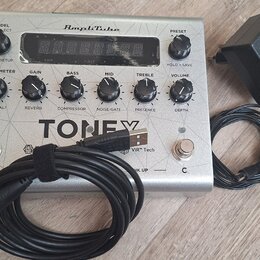 Stříbrný kytarový procesor s nápisy AmpliTube a TONEX v doprovodu černého napájecího adaptéru a kabelu. Zařízení obsahuje digitální displej, několik…