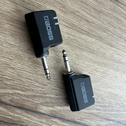 Dvě černé plastové sluchátkové zesilovače s jack konektory. Na obou je bílý nápis BOSS a u horního kusu jsou viditelné nápisy POWER a VOLUME. Povrch…