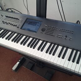 Šedý digitální klavír s černými a bílými klávesami, umístěný na černém stojanu. Na pravé straně jsou bílé nápisy KRONOS MUSIC WORKSTATION a KORG. Nás…