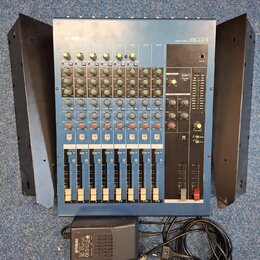 Modrý mixovací pult s nápisem YAMAHA a označením modelu MG12/4. Zařízení obsahuje několik kanálů s posuvníky, otočnými knoflíky a tlačítky v červené…