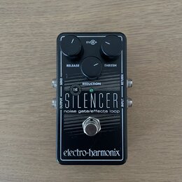 Černý efekt pedál s nápisy THE SILENCER a noise gate/effects loop. Na horní části jsou dva ovládací knoflíky s popisky RELEASE a THRESH, uprostřed je…