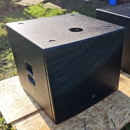 Černý subwoofer v kostkovém provedení s texturovaným povrchem. Přední strana je kryta kovovou ochrannou mřížkou, na které je umístěno malé logo JBL.…
