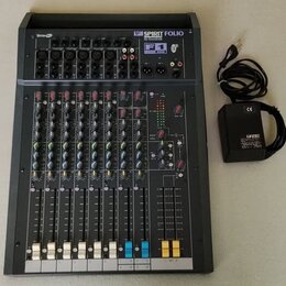 Šedý mixážní pult s nápisem SPIRIT FOLIO by TASCAM a označením F1. Zařízení obsahuje několik vstupních kanálů s posuvníky, knoflíky a kontrolkami. Ve…