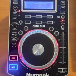 Stříbrný DJ player s černými ovládacími prvky a velkým jog-wheel s červeným podsvícením. Na přístroji jsou nápisy NDX 400, PROFESSIONAL TABLETOP CD /…