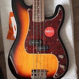 Elektrická basová kytara s korpusem v barevném přechodu od černé přes červenou k žluté. Nástroj má tmavě červený vzorovaný pickguard, na kterém je na…
