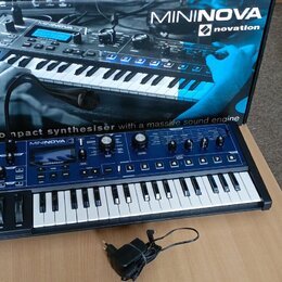Modrý kompaktní syntetizátor s bílými klávesami a černými ovládacími prvky. Na přístroji je nápis MININOVA 2 a logo novation. Syntetizátor stojí před…
