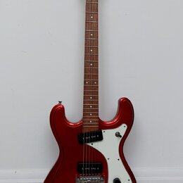 Elektrická kytara s červeným metalickým povrchem těla a hnědým hmatníkem. Na hlavě je bílý nápis "Cort". Kytara má bílý pickguard, jeden snímač typu…