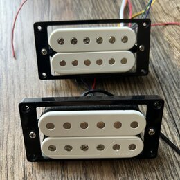 Dvě bílé humbucker snímače v černých plastových rámečkách s přiloženými barevnými vodiči. Na spodním snímači je vpravo vyryt nápis FISHMAN. Povrchy j…