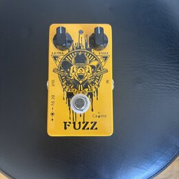 Žlutý efekt pedál s nápisy LEVEL a FUZZ u dvou černých ovládacích knoflíků. Uprostřed je grafika medvěda v klobuku s nápisem FUZZY BEAR a v dolní čás…
