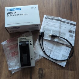 Na fotografii je stříbrný pedál BOSS DUAL FOOT SWITCH FS-7 s dvěma černými spínači. K pedálu patří původní bílá krabice s nápisy BOSS FS-7 DUAL FOOT…