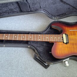 Elektrická kytara s trupem v přechodové barvě od žluté po tmavě hnědou, umístěná v černém tvrdém kufru. Nástroj má dva humbuckery a most s vibrační p…