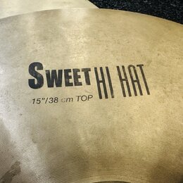 Detailní pohled na mosazný činel s viditelným broušením povrchu. Na čineli je černý nápis SWEET HI HAT a pod ním text 15"/38 cm TOP. Povrch vykazuje…