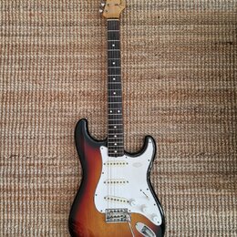 Elektrická kytara typu Stratocaster s barevným přechodem korpusu od černého přes červený k žlutému. Na hlavě hmatníku je viditelné logo Fender. Kytar…