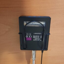 Černý plastový bezdrátový vysílač s připojeným mikrofonem. Na spodní straně je fialová nálepka s nápisy PT 40 FLEXX, Band 40/G, ch1 812.700 MHz, ch2…
