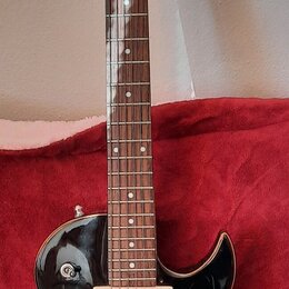 Černá elektrická kytara s tmavým hnedým hmatníkem a bílými tečkovanými značkami poloh. Nástroj má dva humbuckery s krémovými rámečky, stříbrný kobyln…