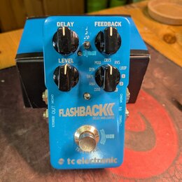 Modrý efekt pedál s nápisy FLASHBACK, DELAY AND LOOPER a tc electronic. Na horní části jsou čtyři černé ovládací knoflíky s popisky DELAY, FEEDBACK,…