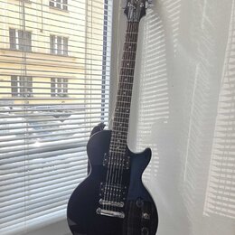 Tmavě modrá elektrická kytara typu Les Paul s černým hmatníkem a stříbrným hardwarem. Na hlavě je bílý nápis Epiphone a logo Spiral. Kytara má dva hu…
