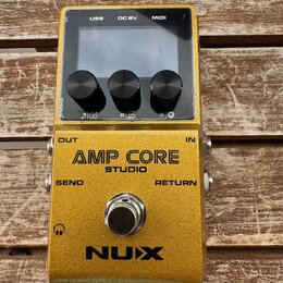 Zlatý efekt pedál s nápisy AMP CORE STUDIO a NUX. Horní část obsahuje displej, tři černé ovládací knoflíky a konektory USB, DC 9V a MIDI. Na spodní č…