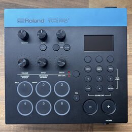 Černý trigger modul s modrým horním panelem. Na modré části je bílý nápis Roland TRIGGER MODULE TM-6 PRO. Zařízení obsahuje displej, několik otočných…