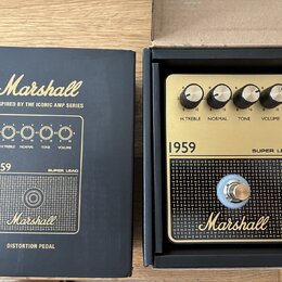 Černá krabice a v ní umístěný zlatý distortion pedál značky Marshall. Na pedálu jsou čtyři černé otočné ovladače s nápisy H.TREBLE, NORMAL, TONE a VO…
