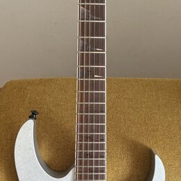 Elektrická kytara s bílým třpytivým povrchem těla a hnědým hmatníkem. Na hlavě je černý nápis Ibanez. Nástroj má tři humbuckery, tremolo mechanismus…