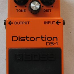 Oranžový efekt pedál s nápisy Distortion a DS-1. Na horní části jsou tři ovládací knoflíky s popisky TONE, LEVEL a DIST a červená kontrolka CHECK. Ve…