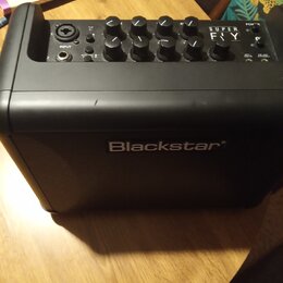 Černý kombozesilovač značky Blackstar. Na horním ovládacím panelu je nápis SUPER FLY, vstup INPUT a několik ovladačů. Přední mřížka má doprostřed umí…