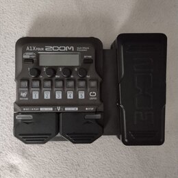 Černý multi-efektový procesor s nápisy A1X FOUR, ZOOM a Multi-Effects Processor. Zařízení obsahuje displej, několik ovládacích tlačítek s popisky jak…