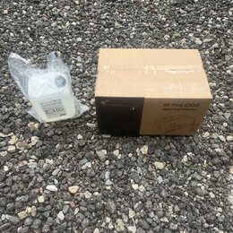 Kartonová krabice s nápisy STARVLUX, M-Fog 1000 a DMX Fog Machine. Vedle krabice je plastová láhev s bílou tekutinou v průhledném sáčku, na které je…