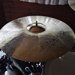 Zlatavý činel s viditelným broušením povrchu. Na pravé straně je nápis istanbul Agop Handmade Turkey. V horní části je vyryto trojúhelníkové logo. Či…