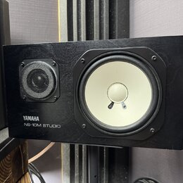 Černý studiový monitor s dřevěným povrchem. Na přední straně je bílý basový reproduktor a menší výšek s kovovou mřížkou. V levém dolním rohu je bílý…